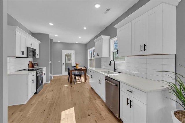 kitchen featuring light wood finished floors, a sink, stainless steel appliances, white cabinets, and light countertops