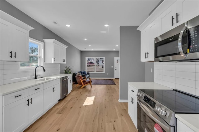 kitchen with a sink, stainless steel appliances, light countertops, light wood-style floors, and white cabinetry