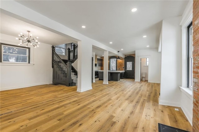 unfurnished living room featuring recessed lighting, stairway, an inviting chandelier, light wood-type flooring, and baseboards