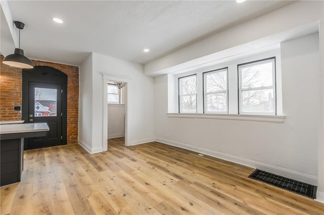 unfurnished living room with light wood-type flooring, brick wall, visible vents, and baseboards