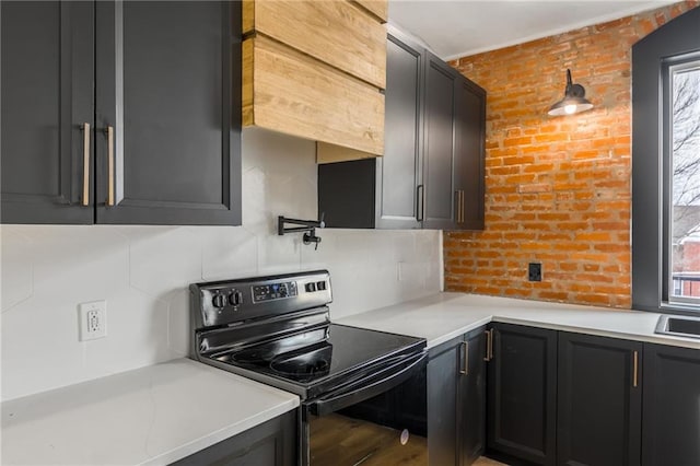 kitchen with dark cabinets, light countertops, black range with electric cooktop, and brick wall