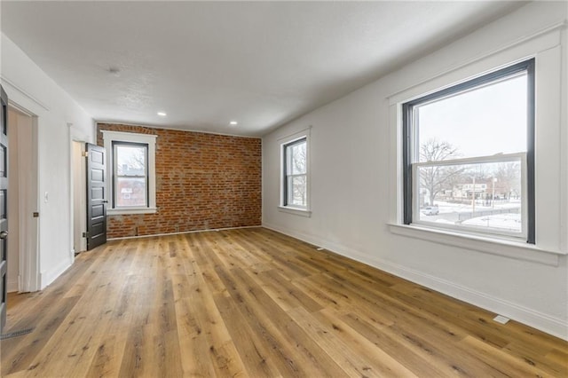 unfurnished room with baseboards, brick wall, recessed lighting, and light wood-style floors