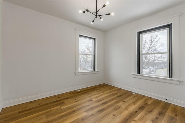 spare room featuring an inviting chandelier, light wood-style flooring, and baseboards