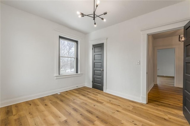 unfurnished bedroom featuring light wood-style flooring, baseboards, and a notable chandelier