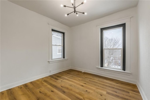 unfurnished room featuring baseboards, light wood-type flooring, and a notable chandelier