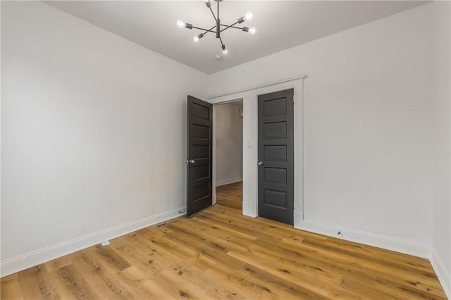 unfurnished bedroom featuring baseboards, light wood-type flooring, and a notable chandelier