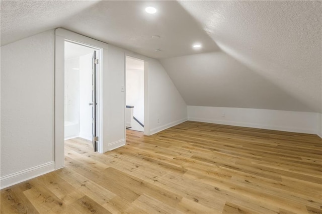 bonus room with a textured ceiling, light wood finished floors, vaulted ceiling, and baseboards