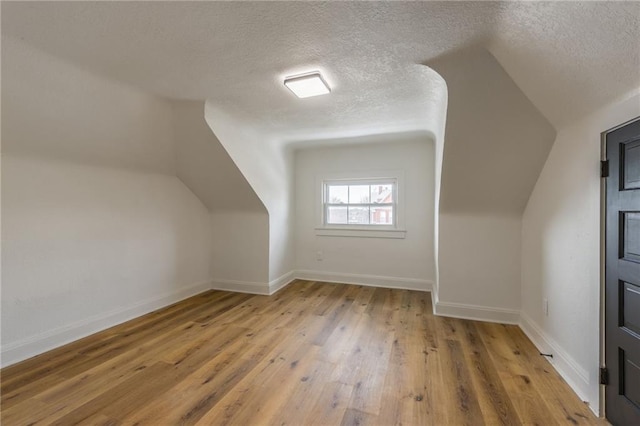 bonus room featuring a textured ceiling, lofted ceiling, hardwood / wood-style flooring, and baseboards