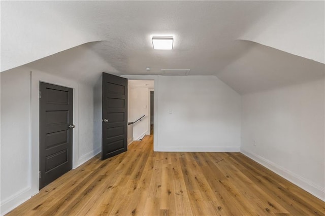 additional living space with light wood-type flooring, baseboards, a textured ceiling, and lofted ceiling