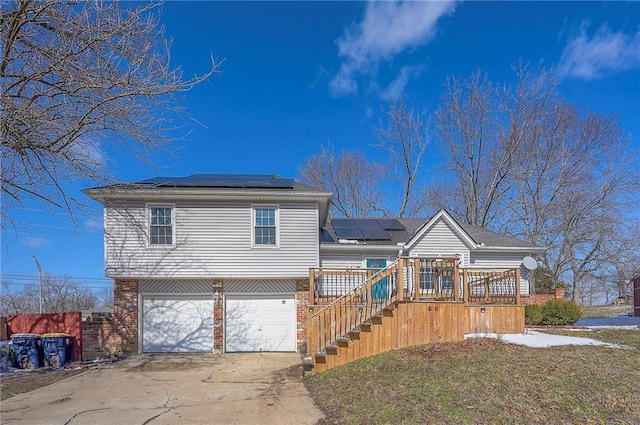 tri-level home with roof mounted solar panels, a front yard, concrete driveway, and brick siding