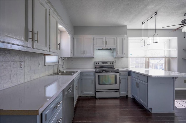 kitchen featuring dark wood-style flooring, a peninsula, stainless steel appliances, light countertops, and a sink