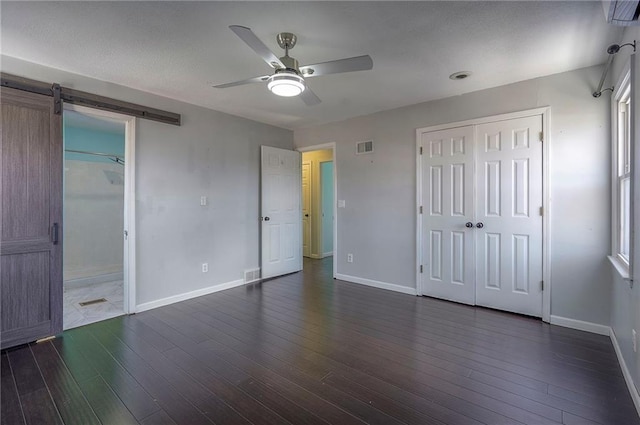 unfurnished bedroom featuring dark wood-style flooring, visible vents, baseboards, and a barn door