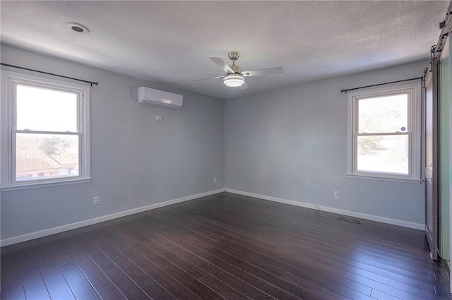 spare room with dark wood-style floors, a wall unit AC, visible vents, and baseboards