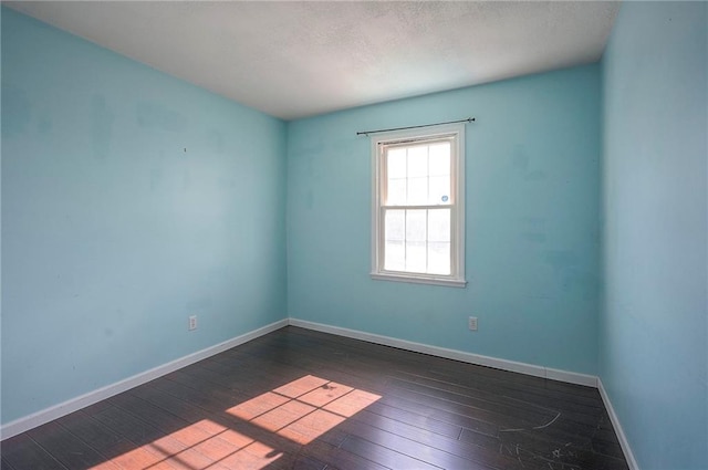 empty room featuring a textured ceiling, dark wood-type flooring, and baseboards