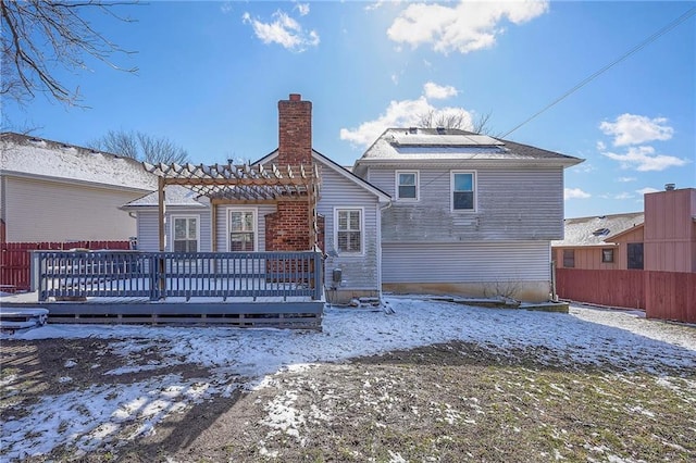 snow covered rear of property featuring a chimney, a wooden deck, and fence