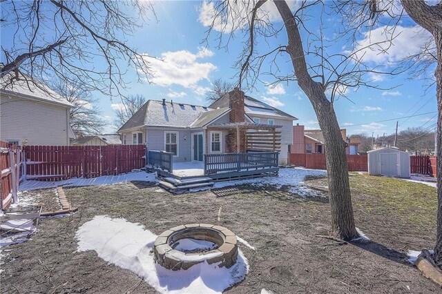 back of property featuring a fire pit, a fenced backyard, an outbuilding, a storage unit, and a wooden deck