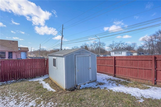 snow covered structure with a storage shed, an outbuilding, and a fenced backyard