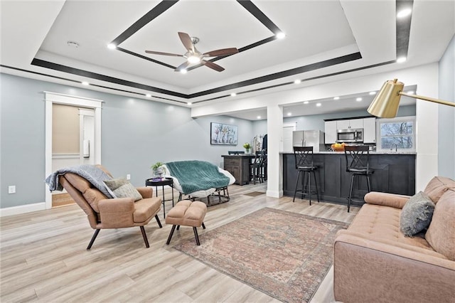 living room with light wood-type flooring, a raised ceiling, and baseboards