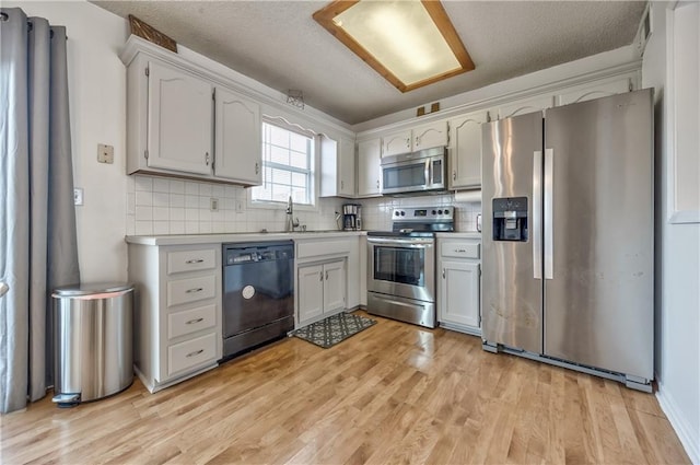 kitchen featuring tasteful backsplash, light countertops, light wood-style flooring, appliances with stainless steel finishes, and a textured ceiling