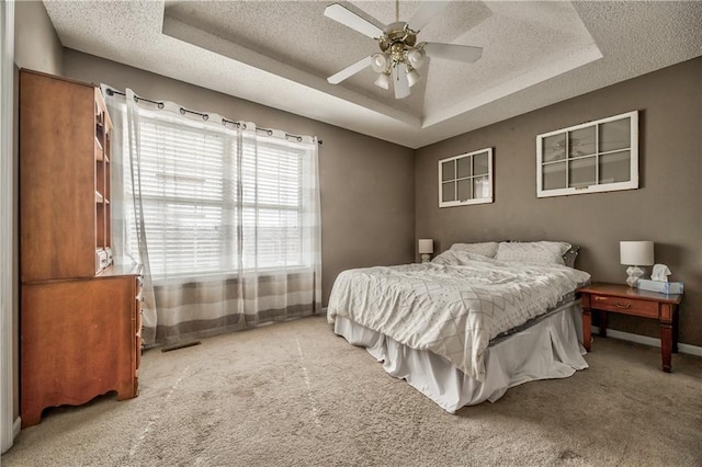 bedroom featuring baseboards, ceiling fan, a tray ceiling, a textured ceiling, and carpet flooring