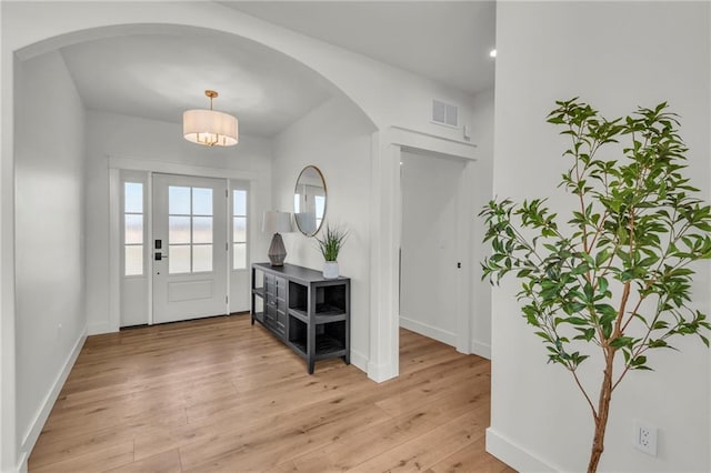 entryway with arched walkways, visible vents, light wood-style flooring, and baseboards