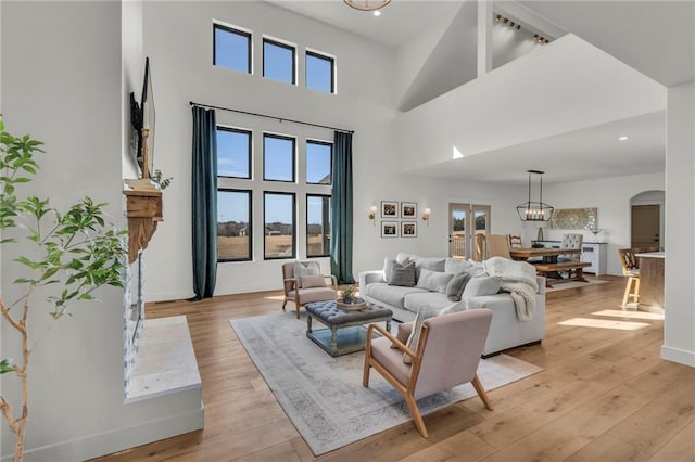 living area featuring light wood-style floors, arched walkways, a towering ceiling, and baseboards