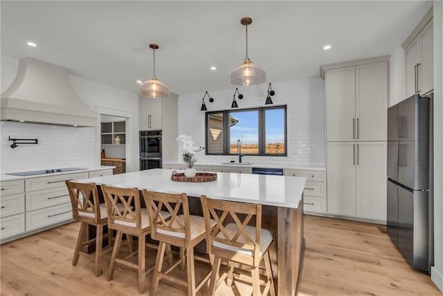 kitchen with light wood-style flooring, freestanding refrigerator, a sink, custom range hood, and double oven