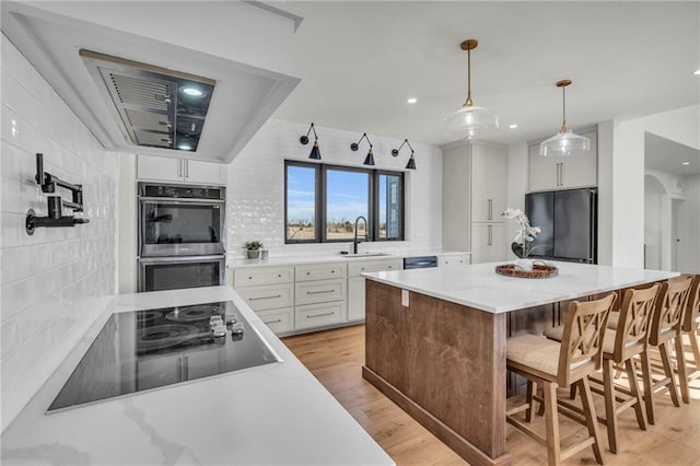 kitchen featuring a sink, decorative backsplash, black appliances, white cabinetry, and light wood-type flooring