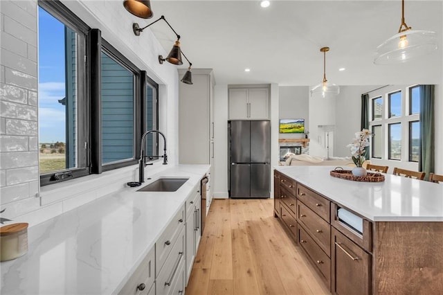 kitchen featuring light wood-style flooring, a sink, freestanding refrigerator, recessed lighting, and hanging light fixtures