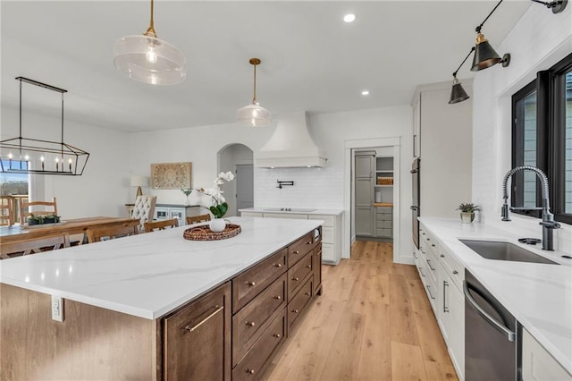 kitchen featuring premium range hood, stainless steel dishwasher, white cabinets, and a sink