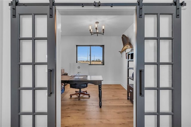 office area featuring a barn door, a notable chandelier, light wood-style floors, and baseboards