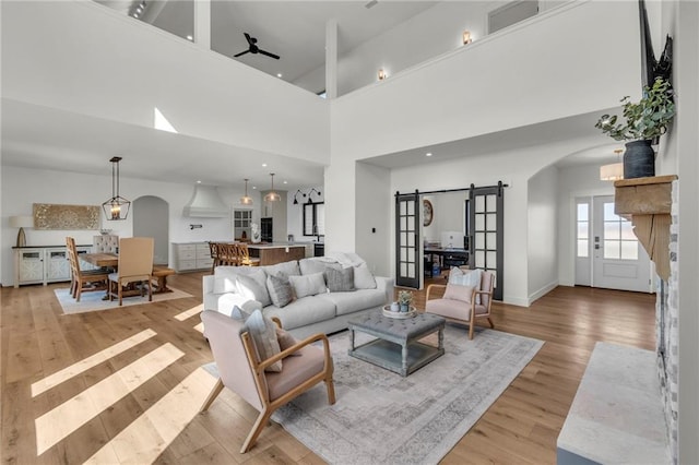 living area with light wood-style flooring, a barn door, arched walkways, a high ceiling, and baseboards