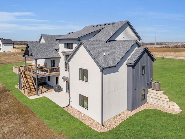 back of property with a lawn, roof with shingles, a wooden deck, central AC unit, and stairs