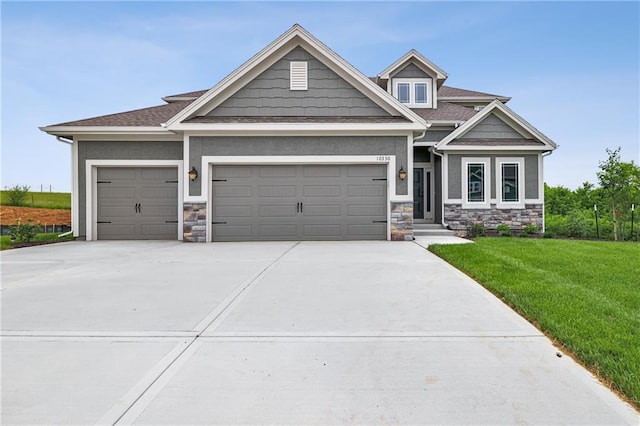 craftsman-style home with stucco siding, a front yard, a garage, stone siding, and driveway