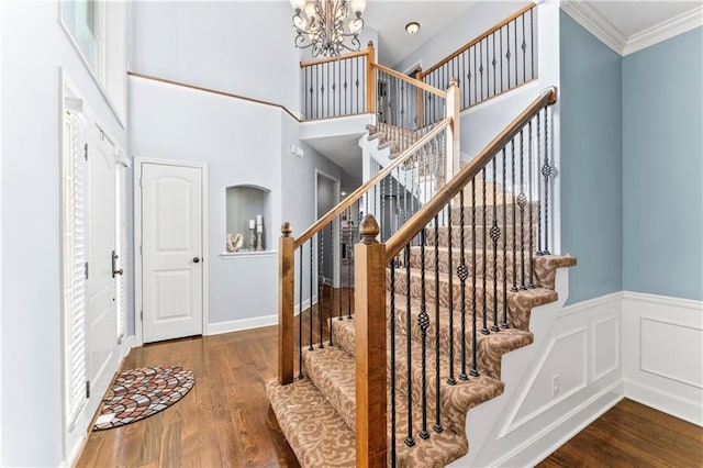 entrance foyer with stairway, wood finished floors, a wainscoted wall, ornamental molding, and a chandelier