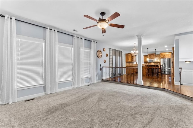 unfurnished living room featuring visible vents, ceiling fan with notable chandelier, baseboards, and carpet