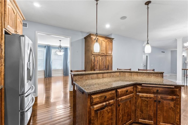 kitchen with visible vents, dark wood-type flooring, stainless steel refrigerator with ice dispenser, dark stone counters, and hanging light fixtures