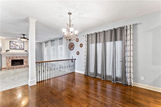 interior space featuring a stone fireplace, ceiling fan with notable chandelier, baseboards, and hardwood / wood-style floors