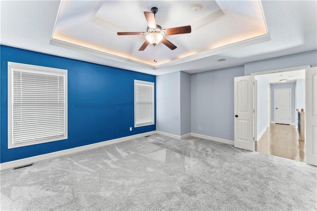 carpeted spare room with visible vents, baseboards, a raised ceiling, and ceiling fan