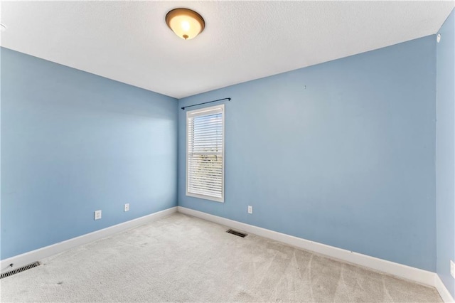 carpeted spare room featuring visible vents, a textured ceiling, and baseboards