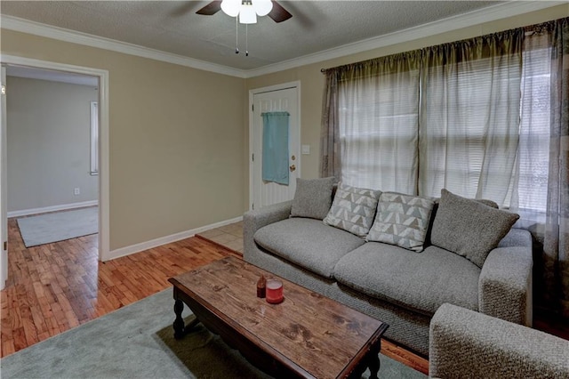 living room with baseboards, ceiling fan, wood finished floors, a textured ceiling, and crown molding