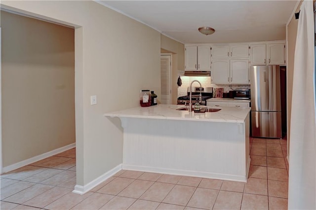 kitchen with light tile patterned floors, decorative backsplash, freestanding refrigerator, a peninsula, and a sink