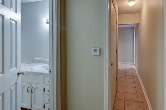 corridor with light tile patterned floors, a textured ceiling, a sink, and baseboards