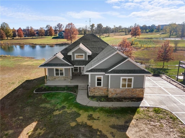 view of front of property with stone siding, a shingled roof, a front lawn, and a water view