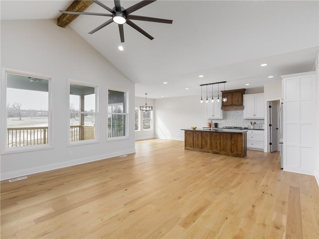 unfurnished living room featuring visible vents, beam ceiling, light wood-style flooring, ceiling fan with notable chandelier, and baseboards