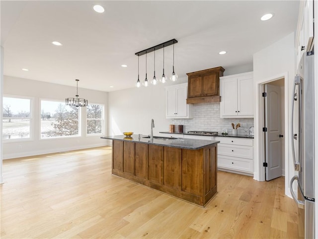 kitchen with light wood-type flooring, decorative backsplash, appliances with stainless steel finishes, white cabinets, and a sink