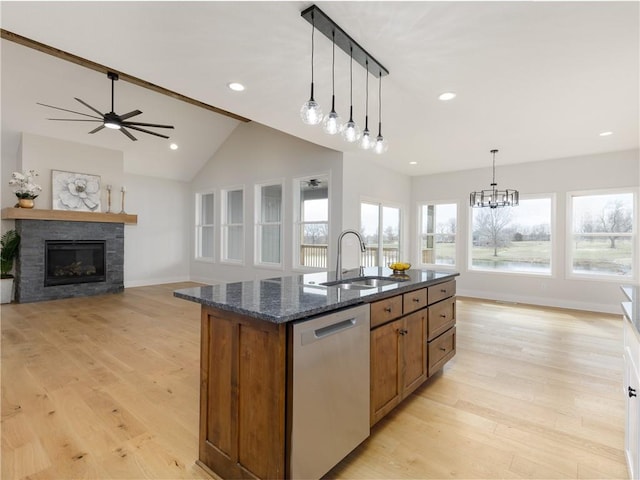 kitchen featuring light wood finished floors, a center island with sink, a stone fireplace, stainless steel dishwasher, and a sink