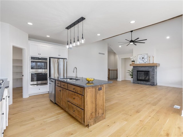 kitchen featuring dark stone countertops, a center island with sink, stainless steel appliances, a sink, and white cabinets