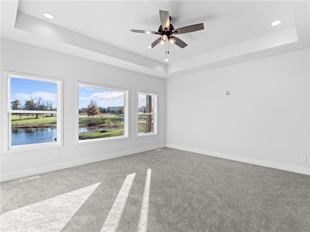 empty room with a raised ceiling, visible vents, baseboards, and carpet floors