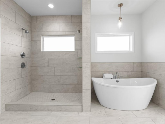 full bathroom with a wealth of natural light, tiled shower, a freestanding bath, and tile walls